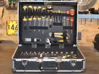 Ein offener Werkzeugkoffer mit verschiedenen Werkzeugen liegt auf einem Holztisch in einer Werkstatt.