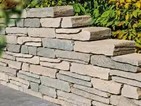 Eine gestapelte Steinmauer steigt in einem Garten vor einem Hintergrund aus grünen Blättern an.