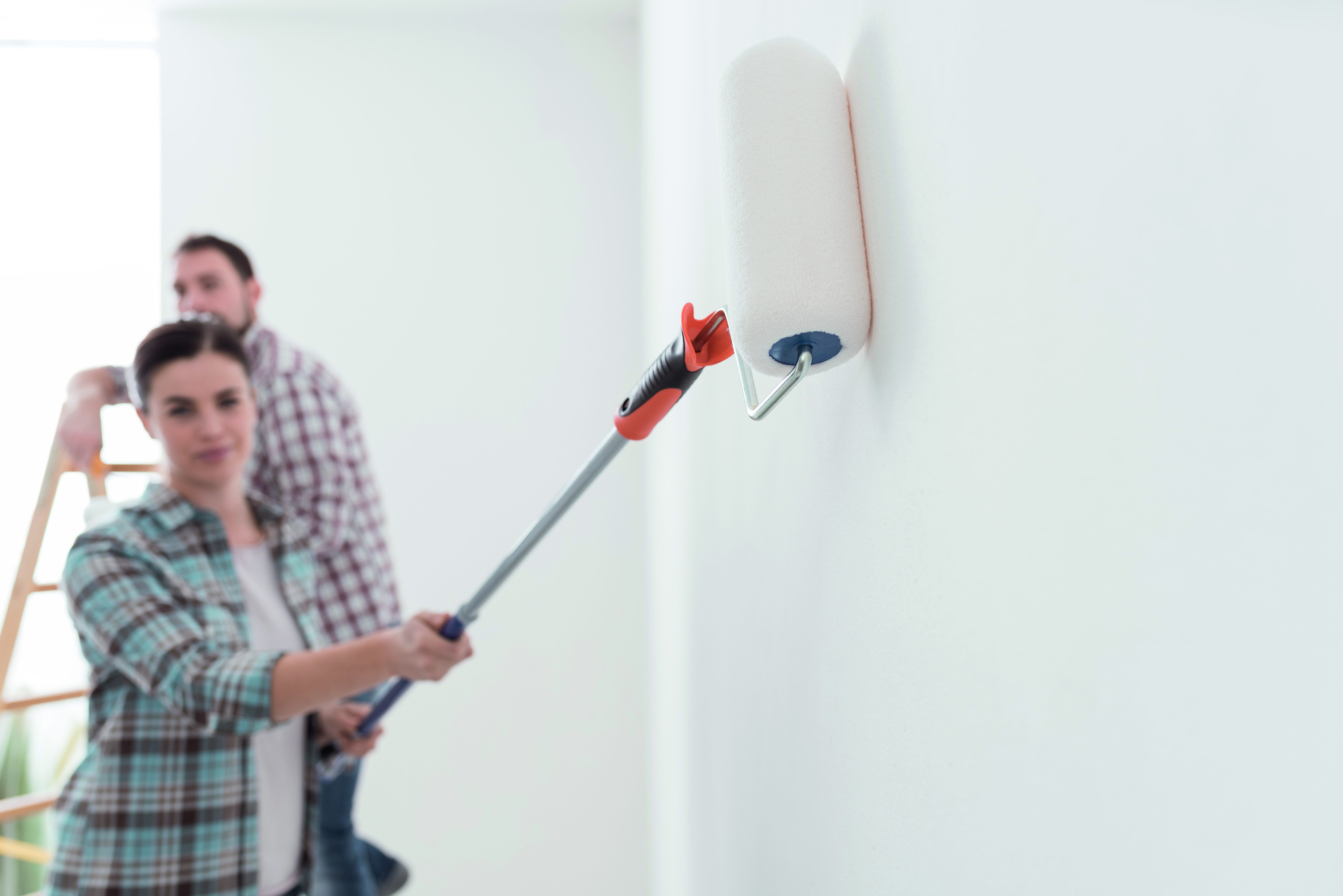 Eine Frau die eine Wand mithilfe eines Teleskobstab streicht