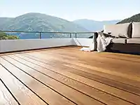 Eine Holzterrasse erstreckt sich neben einem Terrassensofa, umgeben von Bergen und blauem Himmel.