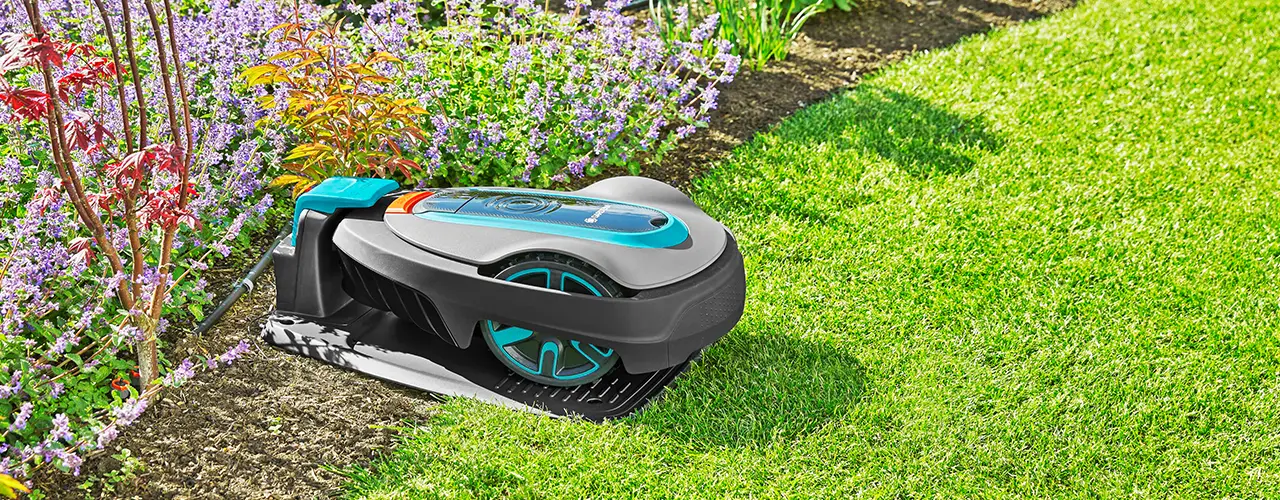 Ein automatischer Rasenmähroboter von Gardena lädt an seiner Ladestation im Garten.