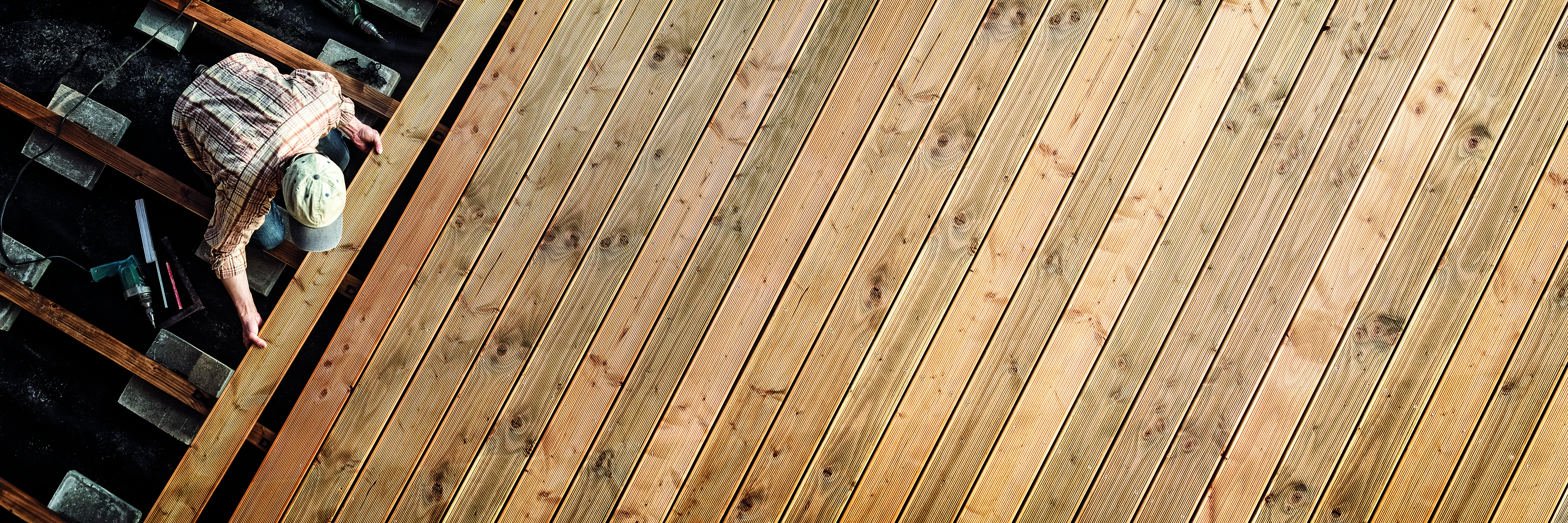 Holzterrasse die gerade gebaut wird wo ein Mann eine Holzdiele einsetzt