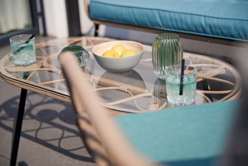 Ein Glastisch mit Getränken, einem Dekanter und einer Obstschale, umgeben von türkisfarbenen Polsterstühlen.