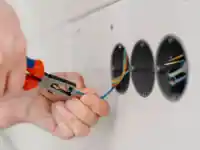 Eine Person zieht mit einer Zange Drähte aus einer Wandöffnung.