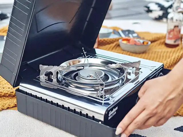 Ein tragbarer Gaskocher wird von einer Hand auf einem Tisch im Freien benutzt.