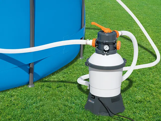 Eine Sandfilterpumpe reinigt Wasser in einem blauen Aufstellpool auf einer grünen Wiese.