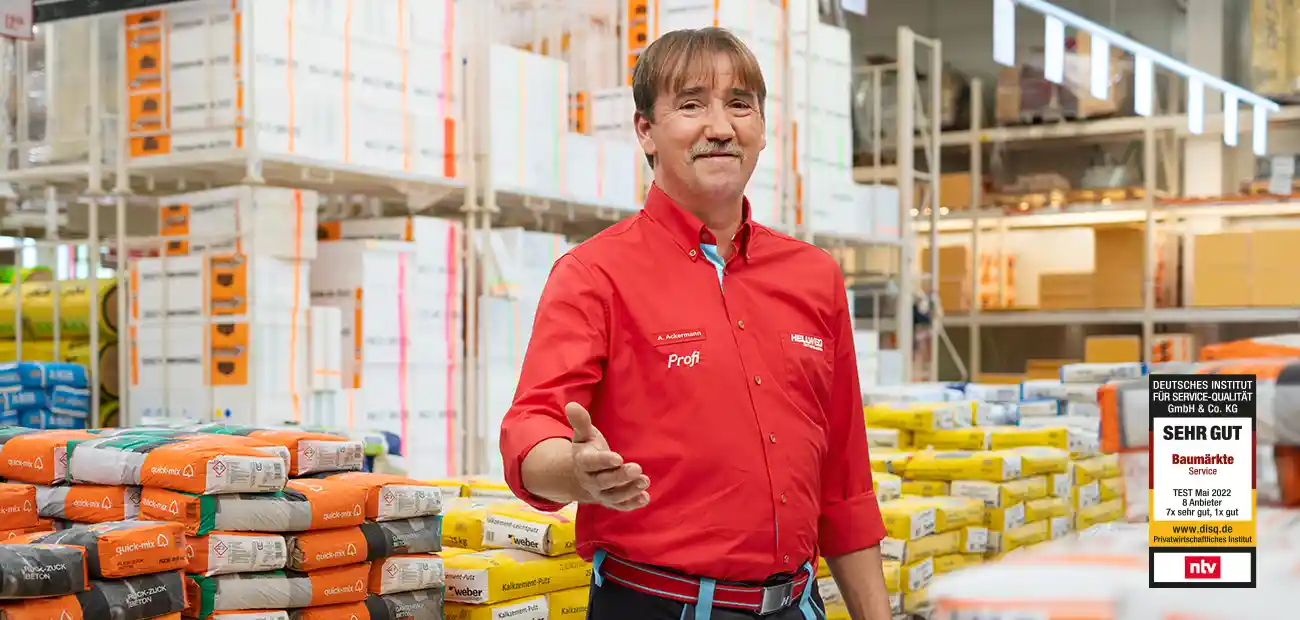 Ein Mann in rotem Hemd steht lächelnd in einem Hellweg Baumarkt.