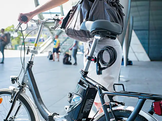 Eine Person hält ein Fahrrad im städtischen Bereich nahe einer modernen Gebäudestruktur.